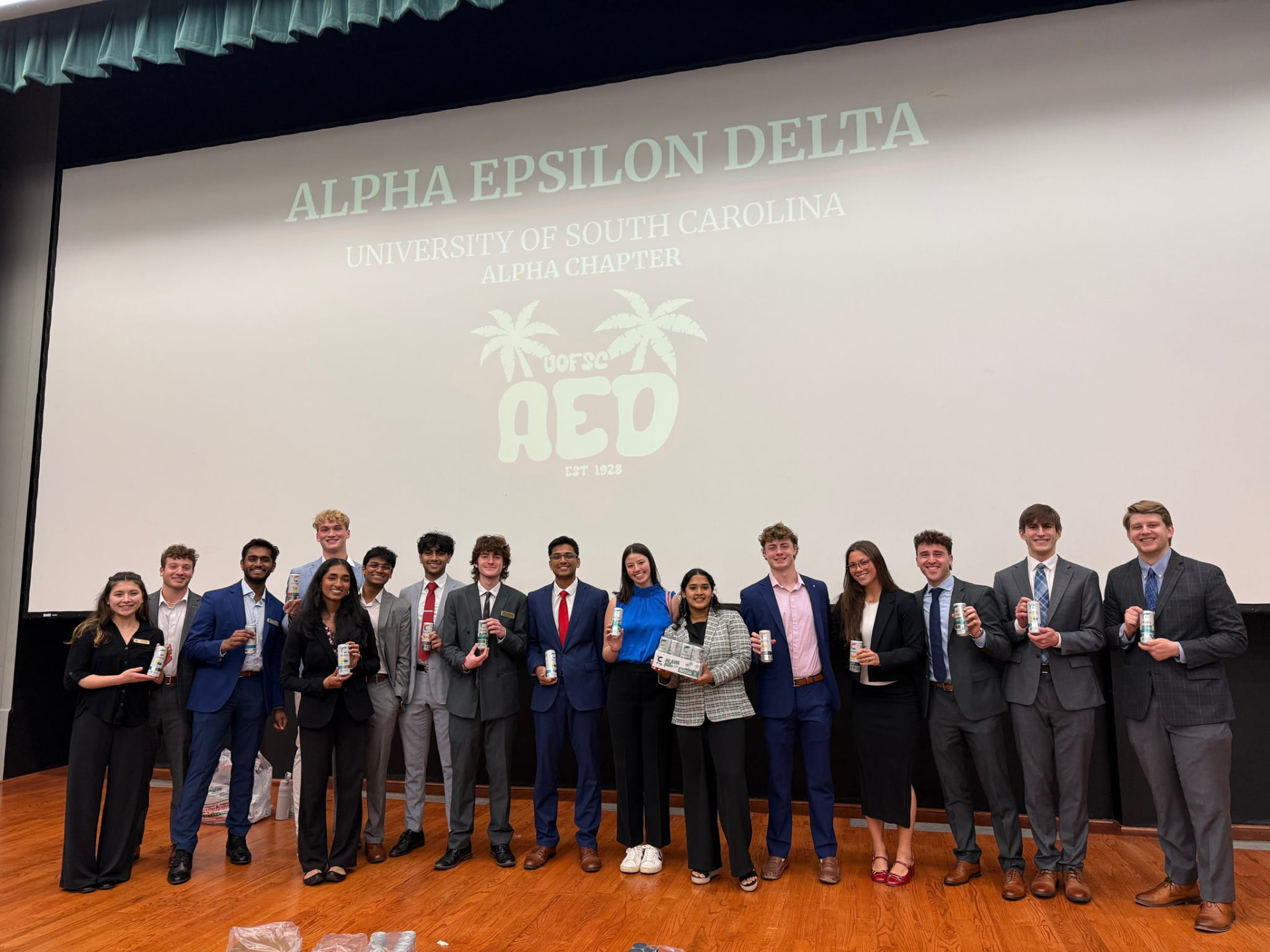AED members in professional attire on stage at a chapter meeting in front of the Alpha Epsilon Delta USC Alpha Chapter slide