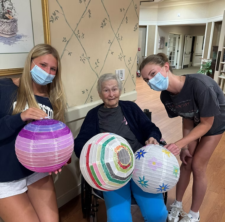 Members holding hand-painted paper lanterns with a resident